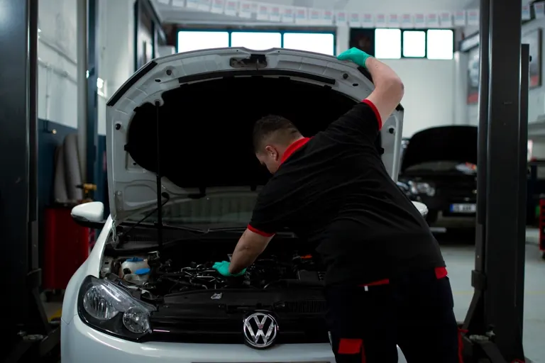 Ein Mechaniker beugt sich in einer Werkstatt über den offenen Motorraum eines Autos.